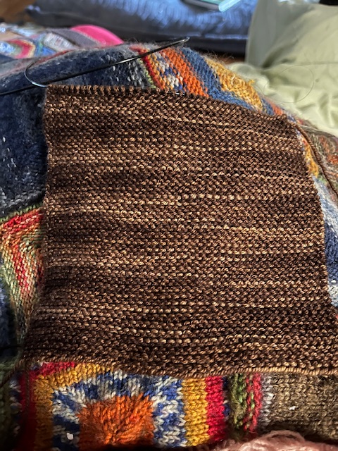 A knitted rectangle in variegated brown yarn. The colors make a kind of sideways zigzag the width of the rectangle.